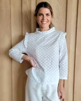 Blusa blanca de manga larga con cuello alto y volados en cuello y hombros.