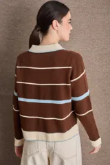 Buzo de punto con cuello polo y cierre frontal de tres botones. Diseño a rayas horizontales en tonos crema, bordó y mostaza, con detalle de bordado en el pecho.