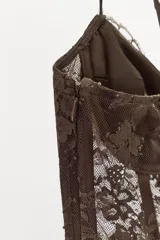 Vestido largo semitransparente confeccionado en encaje con diseño de corsé en el torso, escote con aros, tirantes finos ajustables y cierre frontal con ganchos metálicos.