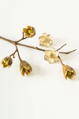 Aros tipo studs con diseño de flor de magnolia en tono crema con centro dorado y detalle de cristales brillantes en uno de los pétalos.