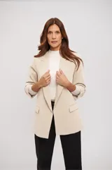 Blazer crudo de corte clásico, diseño abierto con solapas y bolsillos frontales con solapa. Presenta mangas 3/4 con trabilla y botón para arremangar.