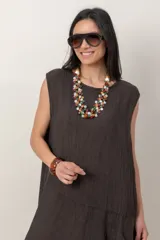 Vestido midi de lino color beige, sin mangas y con cuello redondo. Cuenta con un diseño irregular con detalle de volado vertical a un costado.