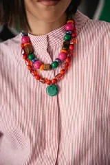 Collar corto compuesto por cuentas de cristal checo en tonos rojos de diversas formas y tamaños, con un medallón central circular de cristal checo en color verde. Incluye cadena de ajuste para regular el largo.