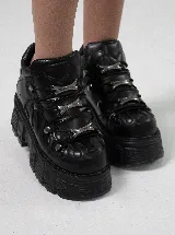 Botas de plataforma estilo chunky color negro, confeccionadas en cuero sintético. Presentan un diseño robusto con suela dentada, cordones negros y detalles metálicos decorativos en el empeine.