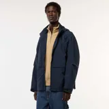 Chaqueta cortavientos azul marino con capucha, cierre frontal y bolsillos con solapa a la altura de la cintura. Presenta un diseño técnico y holgado.