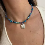 Collar corto de cuentas de colores en tonos azules, violetas y verdes, con dije colgante plateado con forma orgánica.