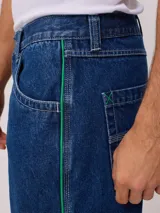 Bermuda de jean de mezclilla negra con efecto lavado, corte recto y costuras en contraste de hilo blanco. Presenta un parche bordado con el logo "Rusty" en color celeste en el bolsillo trasero derecho.