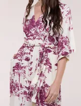 Enterito largo de calce fluido con escote en V cruzado, mangas 3/4 anchas, cintura elastizada con lazo ajustable y pantalón wide leg con bolsillos laterales. Estampado tipo toile de Jouy en tonos violeta sobre fondo blanco.