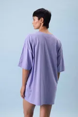 Remera oversize color lila con estampa frontal gráfica en tonos marrón y crema. Presenta cuello redondo, mangas cortas y un corte holgado.