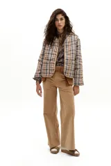 Chaqueta reversible con un lado de twill de lana a cuadros en tonos beige, marrón y gris, con vivos en pana color camel y bolsillos frontales. El otro lado es de algodón capitoneado con estampado de arabescos. Tiene cuello a la base y botones metálicos a presión escondidos.