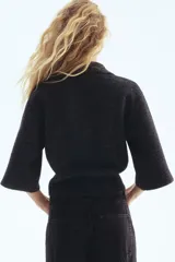 Saco de punto suave color gris oscuro, con cuello camisero y botones frontales. Presenta un diseño de hombros caídos y mangas holgadas que terminan por debajo del codo.