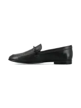 Mocasín de estilo tailor en cuero negro, con costuras marrones visibles alrededor de la puntera y una tira superior con hebilla forrada.