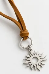 Collar con cordón de cuero tostado y dije metálico de acero en forma de sol.