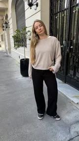 Buzo de punto color beige con textura acanalada, cuello redondo y mangas largas. Presenta un diseño ajustable en los laterales mediante tiras que permiten modificar el largo de la prenda.