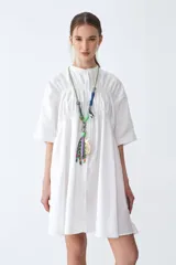 Camisa blanca de poplín de algodón, corte amplio, cuello mao y botones. Tiene recortes con detalles fruncidos en el delantero, espalda y puños.