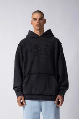 Buzo canguro de corte oversize, confeccionado en frisa de algodón con efecto de lavado gastado. Presenta un aplique decorativo cosido al corte en el centro del pecho, capucha amplia y bolsillo frontal tipo canguro.