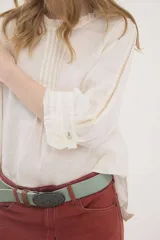 Blusa de lino color marrón, de corte recto y mangas 3/4. Presenta escote redondo con pequeños volados y pliegues frontales, además de detalles de encaje en las mangas y puños con volados.