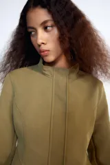Cazadora entallada Zara color verde militar, con cuello alto, manga larga y bajo acabado en peplum. Cuenta con cierre frontal oculto con cremallera y botones a presión.