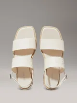 Sandalias planas blancas de cuero sintético, con puntera cuadrada y dos tiras anchas. La tira superior tiene el logo de Calvin Klein grabado.