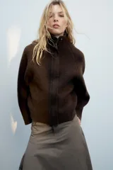Chaqueta de punto marrón de textura bouclé, con cuello subido, manga larga ancha y cierre frontal oculto con cremallera.