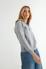 Buzo de punto gris con cuello polo y cierre frontal parcial, de manga larga y diseño holgado con puños y ruedo acanalados.