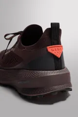 Zapatilla deportiva de correr para trail running, color marrón oscuro. Presenta una parte superior de tejido de punto transpirable, puntera y talón reforzados con material Shield Protect Max. Cuenta con ajuste de cordones, tirador trasero, plantilla OrthoLite® extraíble, entresuela Spume Foam V2 y suela de goma.