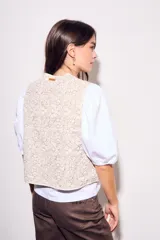 Chaleco sin mangas, color beige claro, con bordados florales en relieve y ribetes a contraste.