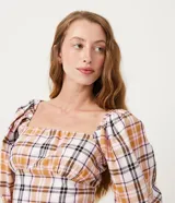 Blusa cropped de algodón con estampado de cuadros en tonos blanco, naranja, marrón y negro. Tiene escote cuadrado, mangas cortas abullonadas y lazo en la espalda.