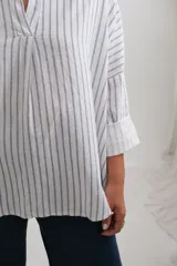Blusa de corte holgado con estampado de rayas verticales azules sobre fondo blanco. Presenta cuello camisero con escote en V y mangas largas amplias con puños vueltos.