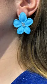 Aros con diseño de flor de cinco pétalos en color celeste, con textura estriada y un pequeño cristal central.