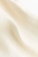 Top fluido de satén color beige, con escote bote, diseño asimétrico y detalles fruncidos en los laterales.
