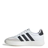 Championes Adidas modelo Barreda, de diseño retro con puntera estilo T-Toe. Presentan una combinación de cuero sintético blanco y detalles en gamuza gris claro, con las icónicas tres tiras laterales en color negro y suela cupsole de goma.