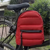 Mochila de nylon color rojo con diseño capitoneado acolchado. Cuenta con un bolsillo frontal con cierre, tiradores metálicos, asa superior y correas ajustables para la espalda.