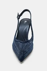 Zapato de tacón alto destalonado con diseño en punta. Presenta una combinación de paneles de mesh transparente y detalles en efecto terciopelo, con tira trasera ajustable mediante hebilla metálica.