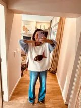 Sweater tejido en hilo de algodón color crudo, con mangas largas de camisa celeste a rayas y aplique de cuero con forma de pez.