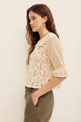 Sweater de tejido calado color beige, con escote en V y mangas cortas abullonadas. Presenta un delicado bordado floral multicolor en la parte frontal superior.