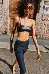 Jeans de tiro medio en denim azul oscuro, con diseño capri de pernera entallada. Presenta cierre frontal con cremallera y botón, y un cinturón integrado con hebilla metálica en la cintura.