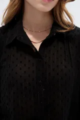 Camisa negra de poliéster con detalles de lurex y textura en relieve, corte holgado, mangas largas con puños y cierre frontal con botones.