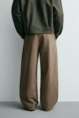 Pantalón de corte baggy fit confeccionado en tejido de algodón con estructura diagonal y efecto lavado. Presenta cintura con pliegues frontales, bolsillos laterales, bolsillos traseros de vivo y un bolsillo lateral adicional con doble vivo en la pernera. Cierre frontal con cremallera y botón.