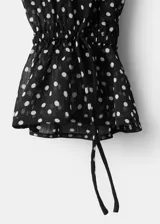 Blusa de poliéster color negro con estampado de lunares blancos, cuello alto con detalle de lazo, manga larga con puños elásticos y diseño recto.
