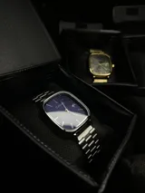 Set de dos relojes de pulsera con caja y malla de acero inoxidable. Incluye un reloj estilo diver con bisel azul y un reloj de esfera cuadrada azul con movimiento de cuarzo.