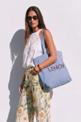 Maxi bolso tipo tote bag de algodón, con diseño de rayas verticales en color azul y blanco. Presenta asas largas para llevar al hombro y el nombre de la marca 'LEMON' impreso en el frente.