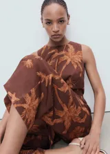 Mono largo marrón con estampado de palmeras, diseño sin mangas, cuello redondo, detalles cut-out en los laterales y un nudo decorativo en la parte delantera.