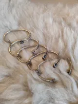 Pulsera rígida de alpaca con detalle central de flor y sección entorchada en tono dorado.