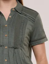 Camisa de manga corta color marrón oscuro, con cuello camisero, alforzas verticales, detalles de puntilla calada y frunces bajo el busto. Cuenta con cierre frontal de botones.