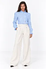 Blusa rosada de 100% lino natural, con cuello alto con volado, mangas largas abullonadas y cierre frontal de botones con detalles de volados en la cartera.
