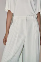Pantalón wide leg de tiro medio, color blanco con diseño de rayas diplomáticas a contraste, bolsillos laterales y de vivo en la espalda, pinzas en el delantero y cierre frontal con cremallera, botón y ganchos metálicos.