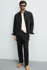 Pantalón negro de corte regular fit, confeccionado en tejido de lino. Presenta cintura con botón y cierre de cremallera, bolsillos frontales y bolsillos traseros de doble vivo.