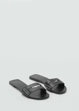 Sandalias planas de cuero negro con tira ancha decorada con costuras visibles y eslabones metálicos plateados.