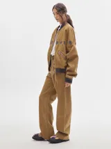 Pantalón jean de tiro alto y corte pinzado, con perneras de caída suelta y levemente anchas en el bajo. Posee pasador con hebilla en la parte trasera.